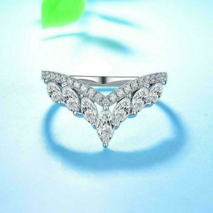 May include: A silver ring with a V-shaped design featuring a row of marquise-shaped clear stones and smaller round clear stones.