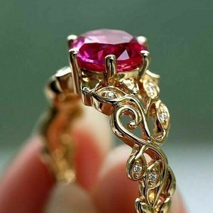 May include: A gold ring featuring a large, oval-cut, pink gemstone. The ring has an ornate, filigree design with small, sparkling accent stones. The band and setting are a warm, polished gold color, creating a luxurious look.