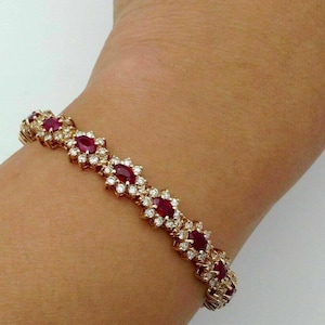 May include: A gold bracelet with a row of oval-shaped red rubies set in a cluster of diamonds.