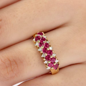 May include: A gold band ring with a row of red ruby stones and smaller white diamonds set in the band.