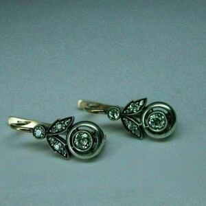 May include: A pair of silver and gold earrings with a floral design and a round diamond in the center of each earring.