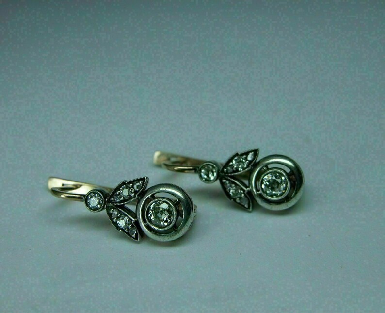 May include: A pair of silver and gold earrings with a floral design and a round diamond in the center of each earring.
