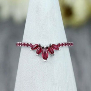 May include: A delicate silver ring with a curved band of small red gemstones and a larger cluster of red gemstones in the center.