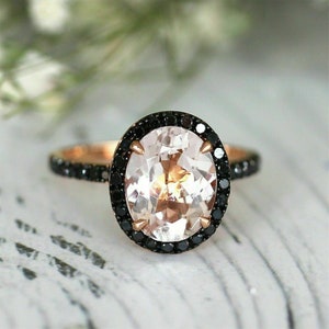 May include: A rose gold ring with a large oval-shaped gemstone surrounded by a halo of black diamonds.
