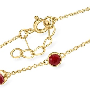 Könnte beinhalten: Ein goldfarbenes Armband mit einer feinen Kette und mehreren runden, roten Edelsteinen. Die Edelsteine sind in goldenen Fassungen gefasst. Der Verschluss und die Verbindungselemente sind ebenfalls goldfarben. Ein klassisches Schmuckstück.