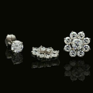 Puede incluir: Tres pares de pendientes de plata con piedras de circonita cúbica transparentes. Los pendientes tienen forma de flor, círculo y una sola piedra.
