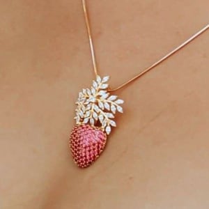 May include: A gold-toned necklace featuring a pendant with a pink, heart-shaped gemstone base. The pendant is adorned with a cluster of white, leaf-shaped embellishments and a delicate chain. The necklace is a piece of jewelry.
