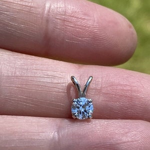 May include: A silver pendant with a clear round gemstone.