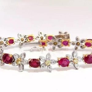 May include: A bracelet with a floral design, featuring oval-cut, deep red gemstones set in silver and gold metal. The bracelet's design incorporates flower-shaped links with small, round yellow gemstones. The clasp is visible.