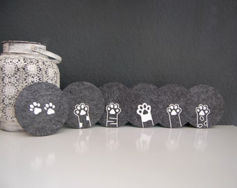 May include: Set of six grey felt coasters with white paw print designs. The coasters feature different paw print designs, including a single paw print, two paw prints, and paw prints with a paw print on the end of a paw.