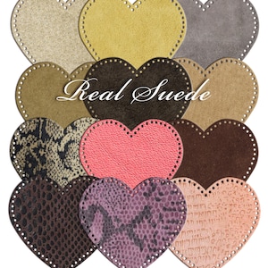 Puede incluir: Un surtido de parches de ante en forma de corazón en varios colores, incluyendo beige, amarillo, gris, marrón, rosa y morado. Algunos corazones presentan patrones texturizados. Las palabras "Real Suede" están escritas en el centro de la imagen.