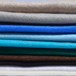 Könnte beinhalten: Ein Stapel Filzstoff in verschiedenen Farben, darunter Weiß, Grau, Blau, Türkis, Grün, Braun und Schwarz.