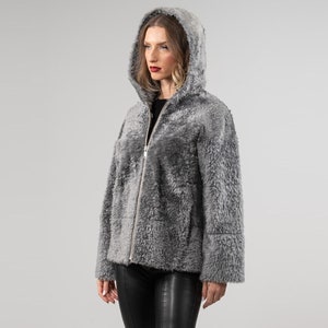 May include: A gray hooded shearling jacket with a zipper closure. The jacket has a soft, fuzzy texture and a relaxed fit.