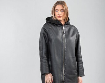 May include: A black hooded shearling jacket with a zipper closure. The jacket has a long, relaxed fit and is lined with a soft, fuzzy material.