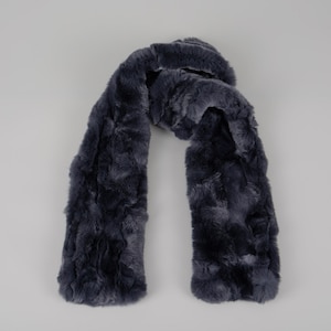 May include: A dark gray faux fur scarf with a textured pattern. The scarf is folded in half and laid flat on a white background.