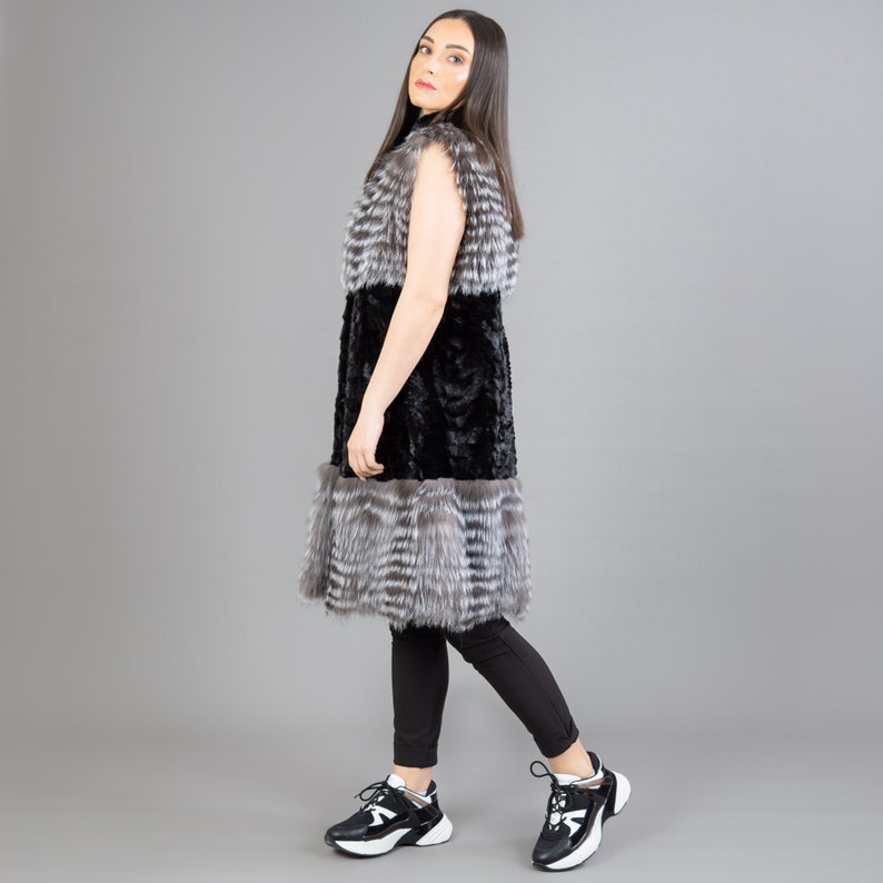 A female model is posing in front of a gray panel. She is wearing a vest made from real fox and mink fur in black and silver colors.