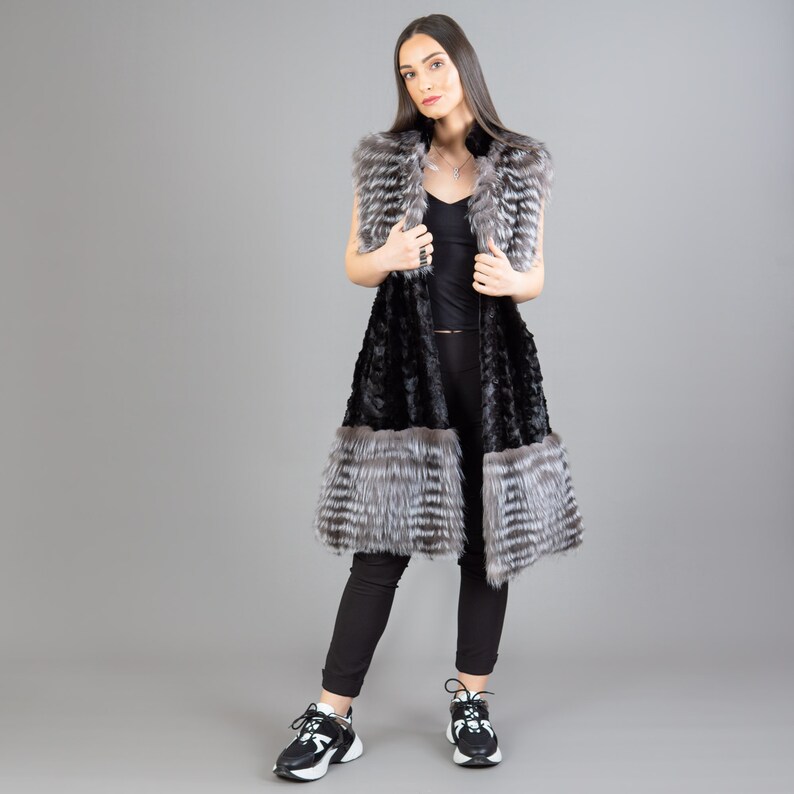 A female model is posing in front of a gray panel. She is wearing a vest made from real fox and mink fur in black and silver colors.