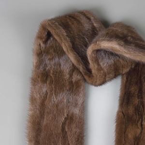 Puede incluir: Una bufanda de piel marr&oacute;n con un dise&ntilde;o largo y fluido. La bufanda est&aacute; hecha de piel suave y lujosa y es perfecta para a&ntilde;adir un toque de elegancia a cualquier atuendo.