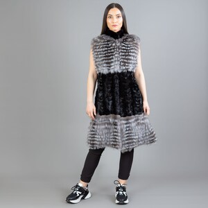 A female model is posing in front of a gray panel. She is wearing a vest made from real fox and mink fur in black and silver colors.