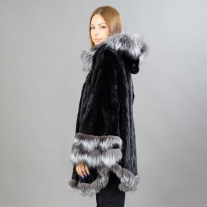 A model posing in front of a gray panel with a black mink fur coat.