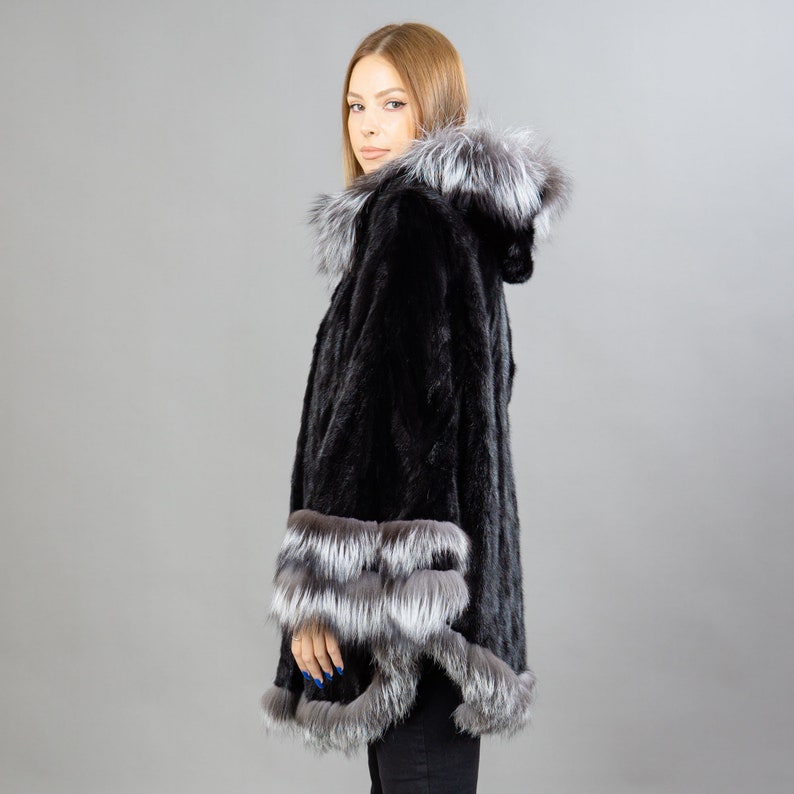 A model posing in front of a gray panel with a black mink fur coat.