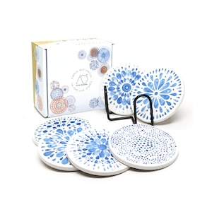 May include: Set of six blue and white ceramic coasters with a watercolor-style design. The coasters are arranged in a circle with a black metal stand in the center. The coasters are packaged in a box with the words "Simple, but special" printed on the side.