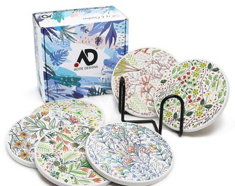 May include: Set of six round ceramic coasters with floral designs in various colors, including green, orange, and blue. The coasters are displayed with a black metal holder and a matching box with the "Acme Designs" logo.