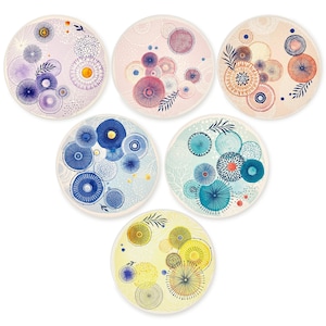 May include: Set of six round coasters with colorful abstract designs. Each coaster features a unique pattern of circles, dots, and lines in shades of blue, pink, yellow, and teal. The coasters have a white border and are suitable for various home decor styles.