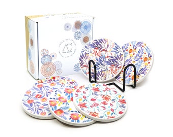 May include: Set of six floral patterned ceramic coasters with a metal stand. The coasters feature a white background with purple, blue, pink, and orange floral designs. The box features the text "Simple but Special, Acme Designs".