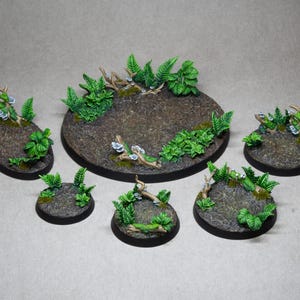 Op de afbeelding: Een verzameling miniatuur terreinbases, met een getextureerd, bruin oppervlak met levendig groen gebladerte en kleine takken. De bases variëren in grootte en vorm, geschikt voor tabletop gaming of model displays.