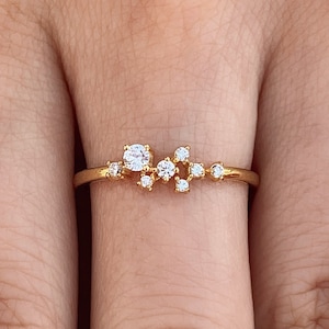 Pu&ograve; includere: Un delicato anello d'oro con un gruppo di piccoli diamanti incastonati in un design minimalista.