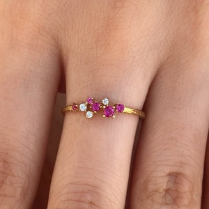 Könnte beinhalten: Ein goldener Ring mit einem Cluster aus rosafarbenen und weißen Edelsteinen. Der Ring wird an einem Finger getragen.