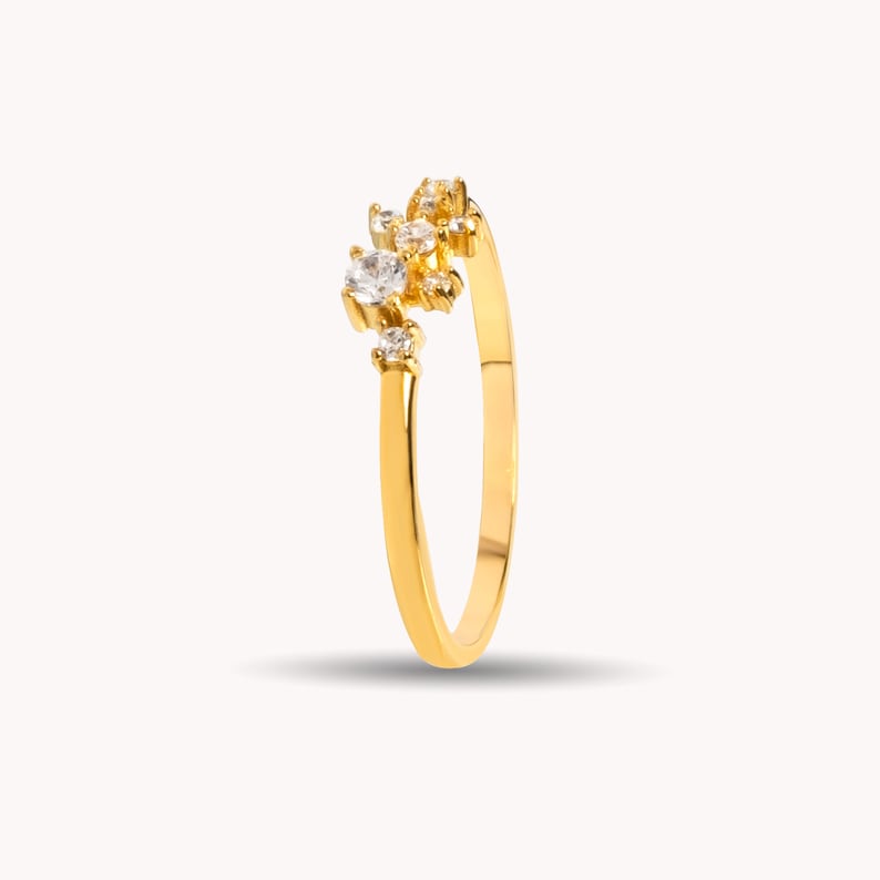 Pu&ograve; includere: Un anello con fascia in oro con un gruppo di piccole pietre preziose trasparenti incastonate nella parte superiore.