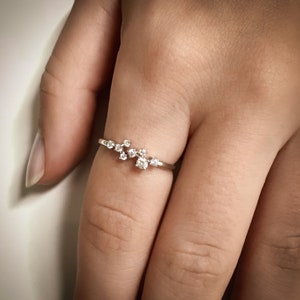 Pu&ograve; includere: Un delicato anello d'argento con un gruppo di piccoli diamanti incastonati in un design delicato e curvo.