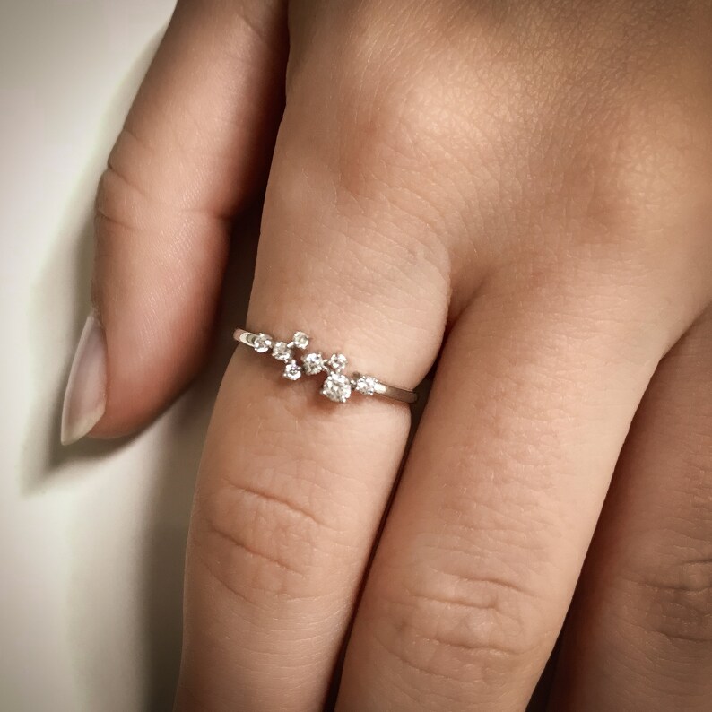 Pu&ograve; includere: Un delicato anello d'argento con un gruppo di piccoli diamanti incastonati in un design delicato e curvo.
