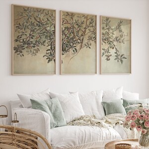 May include: A white sofa with three cushions and a throw blanket, a wooden coffee table with a vase of pink flowers, and three framed botanical prints of green leaves and fruit on a white wall.