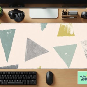 May include: A rectangular desk mat with a cream background and scattered triangles in shades of gray, green, and yellow. A black keyboard and mouse are visible at the bottom, with the "echo desk studio" logo in the bottom right corner.
