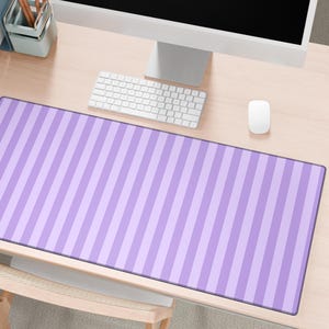 May include: A rectangular desk mat with a vertical striped pattern in shades of purple. The mat is placed on a light-colored wooden desk, alongside a computer, keyboard, and mouse. The desk mat is a decorative and functional office accessory.