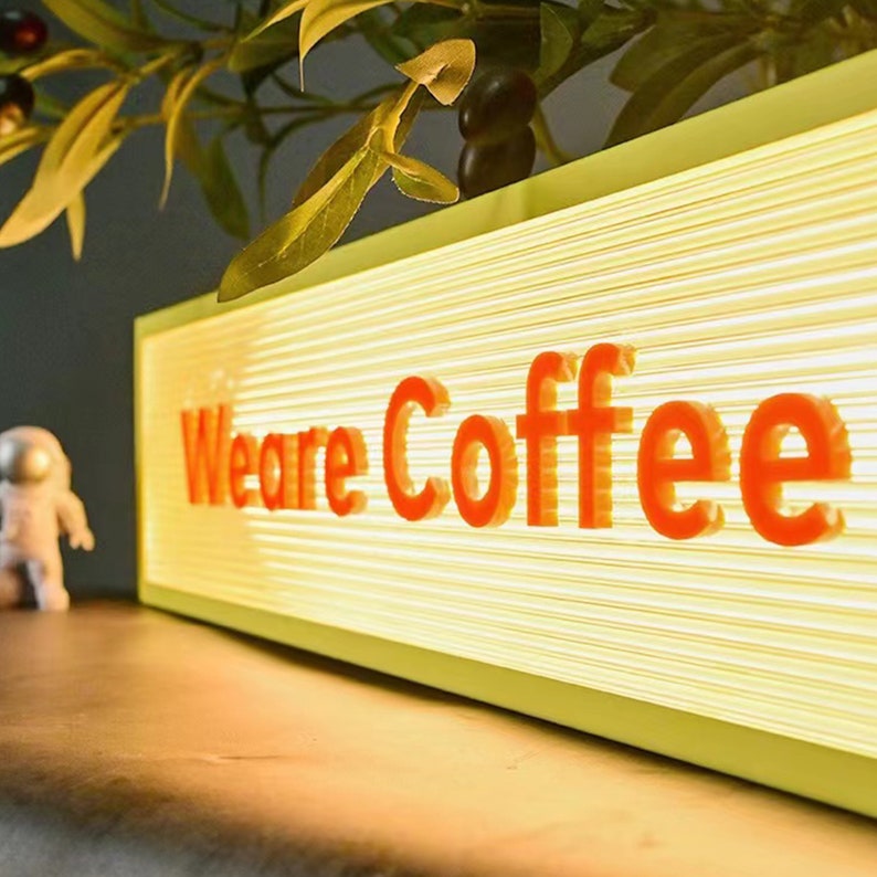 May include: A yellow illuminated sign with the words "We are Coffee" in red lettering. The sign is on a wooden surface.