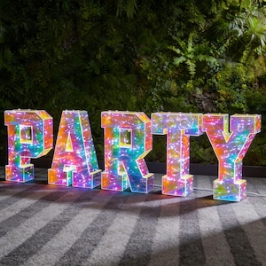 May include: Large, illuminated letters spelling "PARTY" with a rainbow color scheme. The letters are filled with string lights, creating a festive and vibrant display. Perfect for a party or event.