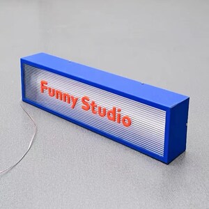 May include: A blue rectangular sign with a white translucent panel and the words "Funny Studio" in red lettering.