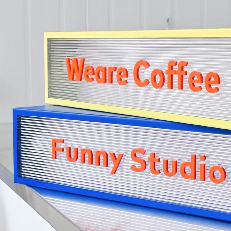 May include: Two illuminated signs stacked on top of each other. The top sign is yellow with the text "We are Coffee" in orange letters. The bottom sign is blue with the text "Funny Studio" in orange letters.