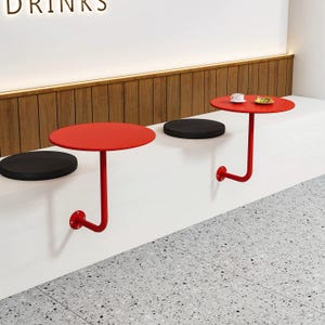 May include: Red, round tables with a J-shaped support are mounted on a white wall. Black, round cushions are placed on the wall. The tables are approximately 24 inches in diameter. The wall has a wooden panel and the floor is gray.