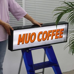 May include: A black and white sign with the text "MUO COFFEE" in orange letters. The sign is sitting on a blue step stool.