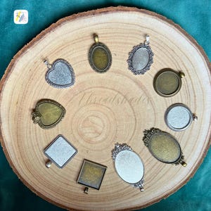 Puede incluir: Una colección de bandejas para colgantes en varias formas, incluyendo corazones, óvalos y cuadrados, con acabados plateados y bronce. Las bandejas están dispuestas sobre una superficie de madera, mostrando su potencial decorativo para la creación de joyas. El texto "Threadshades" es visible.
