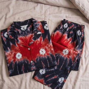 K&ouml;nnte beinhalten: Ein Schlafanzug-Set im Batik-Design in Rot, Marineblau und Wei&szlig;. Das Set beinhaltet ein Hemd mit Kn&ouml;pfen und eine passende Hose. Das Hemd hat einen Kragen und die Hose hat einen elastischen Bund. Der Stoff hat ein einzigartiges, k&uuml;nstlerisches Muster.