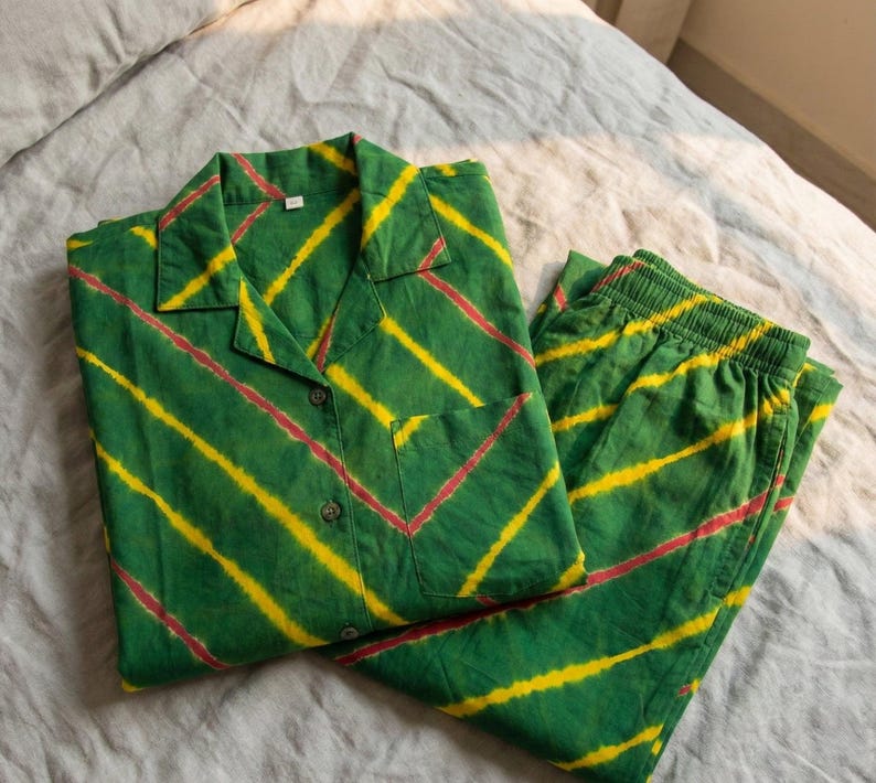 K&ouml;nnte beinhalten: Gr&uuml;nes Pyjama-Set mit gelben und roten diagonalen Streifen. Das Oberteil hat einen Kragen, eine Vordertasche und Kn&ouml;pfe. Die passende Hose hat einen elastischen Bund. Der Stoff scheint Baumwolle zu sein.