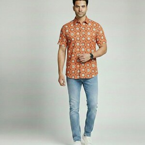 Puede incluir: Una camisa naranja de manga corta con un patr&oacute;n circular repetido en blanco y marr&oacute;n, combinada con vaqueros azul claro y zapatillas blancas. La camisa tiene un cuello cl&aacute;sico y se lleva con un reloj negro.