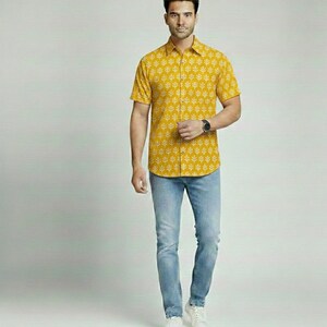 Puede incluir: Camisa amarilla mostaza de manga corta con un estampado de hojas blancas. La camisa se combina con vaqueros azul claro y zapatillas blancas. Un reloj se lleva en la mu&ntilde;eca izquierda. El conjunto es informal.
