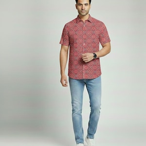 Puede incluir: Una persona con una camisa roja de manga corta con un estampado geom&eacute;trico y vaqueros azul claro. La camisa tiene cuello abotonado y se combina con zapatillas blancas. Se ve un reloj negro en la mu&ntilde;eca.